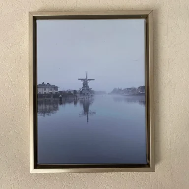 Een windmolen weerspiegeld in een mistige waterweg.