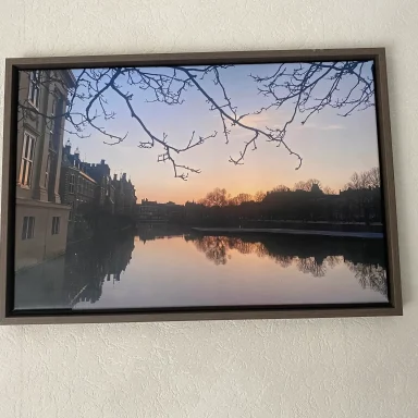 Zonsondergang weerspiegeld in een rustig water met bomen en gebouwen aan de oever.