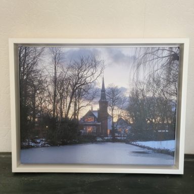 Winterlandschap met een kerk en bomen bij een bevroren vijver tijdens zonsondergang.